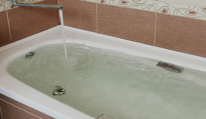 A white bathtub filled with water from a running faucet