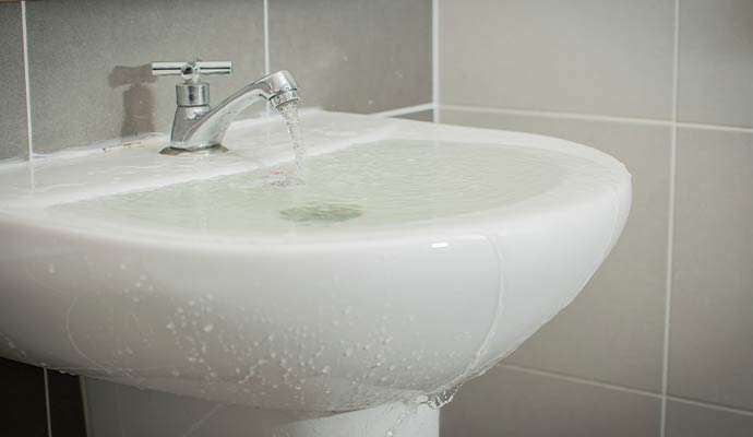 A white ceramic bathroom sink overflowing with water from a running faucet