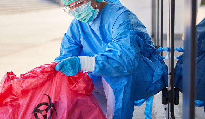 A professional in full PPE handling a red biohazard waste bag during a specialized cleanup