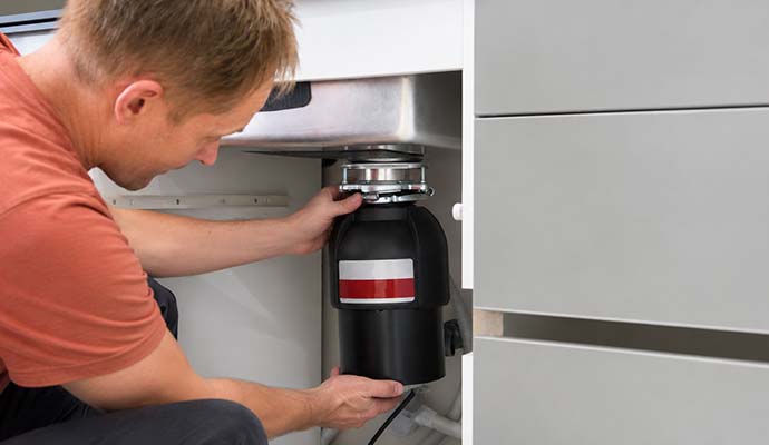 Technician inspecting and maintaining a garbage disposal unit under a kitchen counter