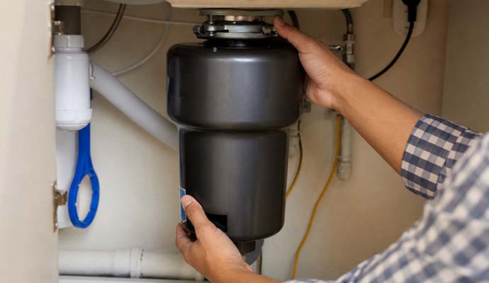 Technician installing a garbage disposal unit under a kitchen sink