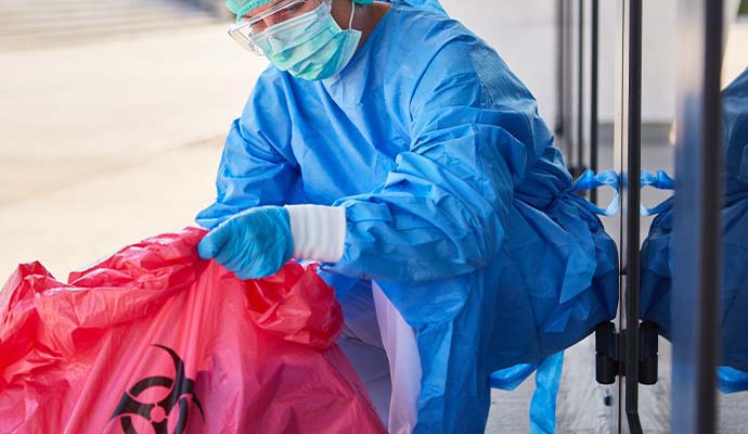 Technician in a protective suit and gloves using a red waste bag for biohazard cleanup