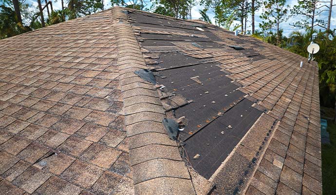 A residential roof with significant wind damage and missing shingles