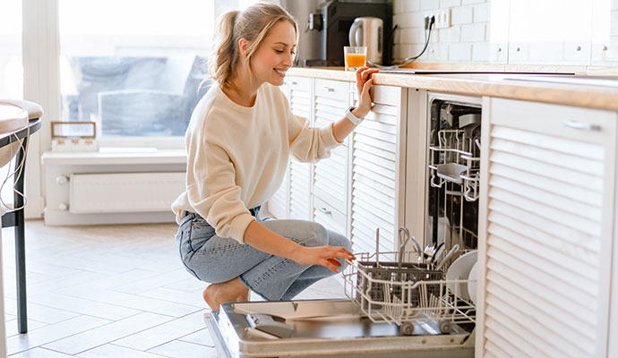 A woman sitting beside a neat and clean dishwasher