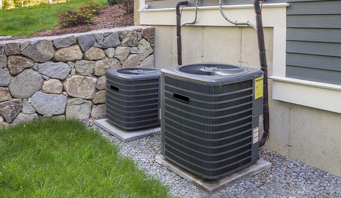 Outdoor central HVAC condenser units installed on gravel beside a residential home
